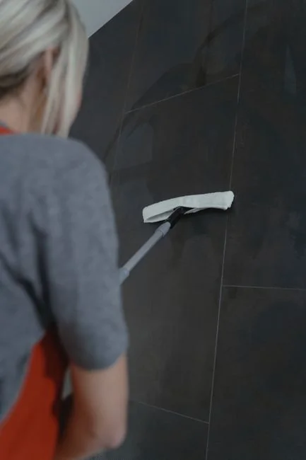Close-up of hand cleaning window with squeegee outdoors using yellow gloves.